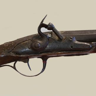 L’image est un détail du fusil à silex offert par le Roi Louis XV au chasseur d’esclaves fugitifs, François Mussard. L’arme a été modifiée. Elle ne fait pas appel à une platine à silex mais à un système à capsule dit à percussion.