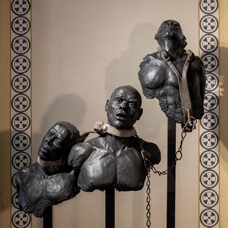La sculpture en terre cuite du buste de trois esclaves portant chacun autour du cou un collier en cuir relié par une chaîne